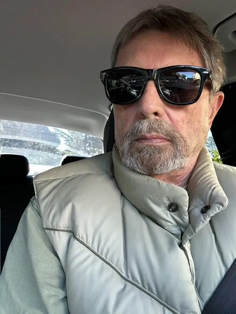 Vernon in his car, in sunglasses and a sage vest